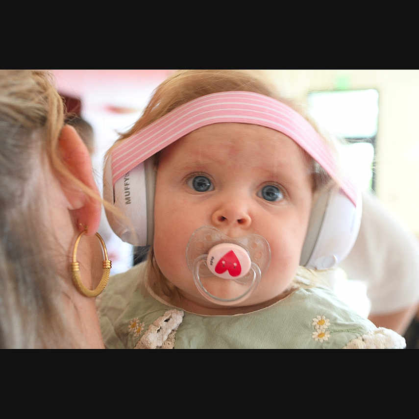 Giorgia participe au concours pour gagner de l'argent avec cette photo : adult, baby, blue_eyes, child, close_up, clothing, curly_hair, cute, earring, expression, face, headphones, holding, indoor, infant, pacifier, person, pink_headband, portrait, soft_light