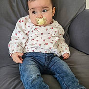 Martina participe au concours pour gagner de l'argent avec cette photo : baby, blue_jeans, casual, child, clothing, couch, curious, cute, face, flower_clip, gray_couch, head, indoors, infant, pacifier, portrait, sitting, small_hands, white_sweater, young_child