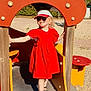 casual_clothing, child, daytime, footwear, girl, happy, hat, nature, outdoor, person, play, playground, red_dress, sand, slide, smiling, summer, sunglasses, sunny, tree
