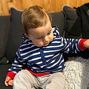 Kleos a rejoint le concours — aidez-le/la à gagner de superbes lots ! toddler, child, striped_hoodie, blue, white, red, couch, pillow, wooden_wall, indoor, sitting, curious, clothing, young_child, portrait, soft_lighting, casual, cozy, baby, furniture