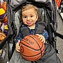 Kleos a rejoint le concours — aidez-le/la à gagner de superbes lots ! toddler, baby, basketball, stroller, child, tongue_out, store, sports_store, basketball_rack, shoe_boxes, carpet_floor, clothing, playful, smiling, indoor, person, face, hand, seated, gray_blanket