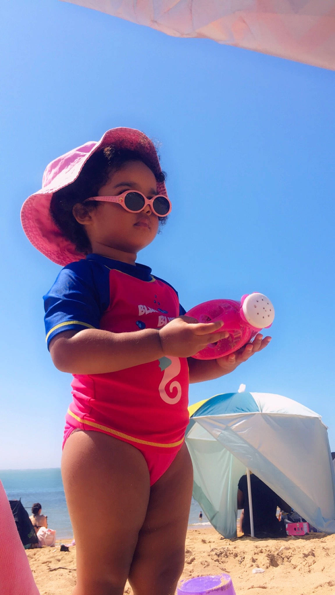 Eléa a rejoint le concours — aidez-le/la à gagner de superbes lots ! azure, beach, blurred, cap, fun, goggles, happy, hat, leisure, light, magenta, people_on_beach, person, photograph, pink, red, sky, summer, sunglasses, tent