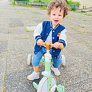 Sahïr participe au concours pour gagner de l'argent avec cette photo : blue_jacket, casual_clothing, child, curly_hair, cute, daylight, fun, green, happy, outdoor, pavement, person, play, smiling, sneakers, toddler, toy, tricycle, white, young_child