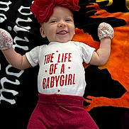 Brooklynn is registered to the contest to win money with this photo: baby, infant, smiling, red_flower_headband, mittens, white_onesie, red_pants, tongue_out, lying_down, colorful_blanket, halloween_theme, orange, black, yellow, cute, child, portrait, happy, playful, indoors
