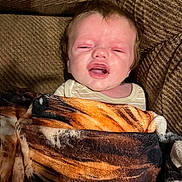 Jaydean is registered to the contest to win money with this photo: baby, blanket, tiger_stripe, couch, fabric, person, infant, face, expression, indoor, comfort, cozy, clothing, head, portrait, young_child, skin, hair, resting, wrapped