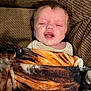 baby, blanket, tiger_stripe, couch, fabric, person, infant, face, expression, indoor, comfort, cozy, clothing, head, portrait, young_child, skin, hair, resting, wrapped