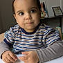 artwork, background, casual, child, crumbs, curly_hair, expression, face, furniture, hands, highchair, home, indoor, long_sleeve, portrait, seated, striped_clothing, sweater, table, toddler
