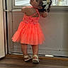 toddler, child, dress, neon, orange, bows, hair, curly_hair, sandals, door, floor, wood_floor, indoor, playful, pose, looking_back, cute, girl, standing, window
