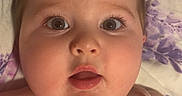 Blair joined the competition — help win amazing prizes! baby, blanket, child, cute, expression, eyelashes, face, floral_pattern, indoors, infant, lying_down, mouth_open, person, pink_clothing, pony_tail, portrait, skin, soft_lighting, wide_eyes, young_child