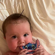 Blair is registered to the contest to win money with this photo: baby, infant, child, cute, cheeks, hair, phone_case, cartoon, stitch, blanket, white, lying_down, hands, face, eyes, playing, indoor, soft_light, skin, adorable