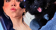 Missy joined the competition — help win amazing prizes! woman, person, puppy, dog, black_dog, pet, car, selfie, portrait, kissy_face, tongue_out, fluffy, bow, purple_bow, blue_outfit, seatbelt, vehicle, indoor, daylight, cuddling