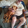 man, dog, couch, cap, glasses, phone, cane, blanket, poster, wooden_cane, shorts, tshirt, footwear, indoor, pet, seated, relaxed, living_room, beard, smiling