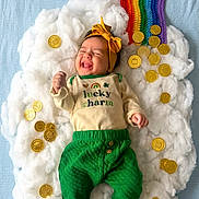 Alice is registered to the contest to win money with this photo: baby, infant, smiling, headband, bow, cloud, cotton, rainbow, gold_coins, onesie, green_pants, bare_feet, lucky_charm_text, top_view, props, newborn, st_patricks_theme, soft_texture, joyful, photography