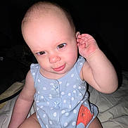 Maeve joined the competition — help win amazing prizes! baby, child, onesie, polka_dot, blue_clothing, sitting, indoor, face, hand, ear, expression, skin, cute, infant, person, playful, portrait, light, dark_background, candid