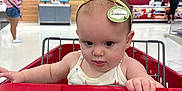 Maeve is registered to the contest to win money with this photo: baby, child, shopping_cart, headbopper, yellow, store, retail, gift_registry, order_pickup, red, tongue, expression, person, indoor, clothing, hand, face, eyes, playful, cute