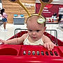 baby, child, shopping_cart, headbopper, yellow, store, retail, gift_registry, order_pickup, red, tongue, expression, person, indoor, clothing, hand, face, eyes, playful, cute