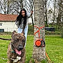 dog, brindle, tongue_out, woman, long_hair, hoodie, jeans, tree, grass, yard, outdoor, playful, leash, leash_holder, house, fence, smiling, spring, nature, pet