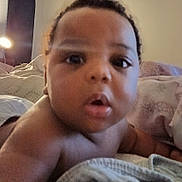 Joshua is registered to the contest to win money with this photo: baby, bed, bedding, bedroom, blanket, child, close_up, cuddly, curious, eyes, face, indoors, infant, photograph, pillow, portrait, puckered_lips, selfie, serious, soft_lighting