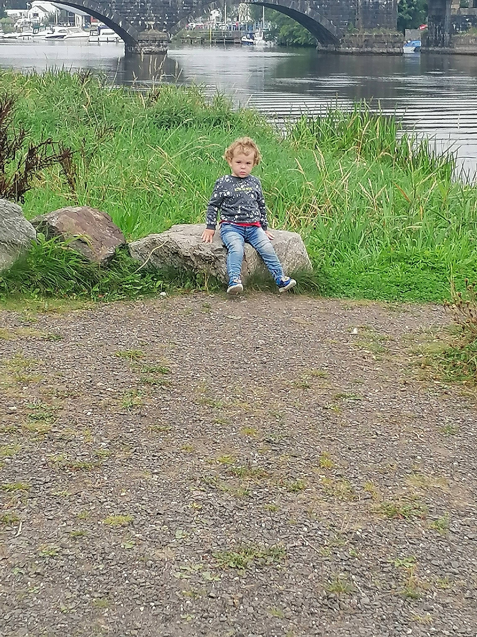 Micheal is registered to the contest to win money with this photo: asphalt, grass, grass_family, grassland, groundcover, lake, landscape, lawn, leisure, people_in_nature, person, plant, recreation, reservoir, rock, sitting, soil, spring, toddler, tree