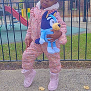 Michelle joined the competition — help win amazing prizes! child, girl, plush_toy, playground, fence, slide, boots, pink_outfit, curly_hair, hair_puffs, outdoor, grass, trees, cloudy_sky, side_gaze, toy, winter_clothing, urban, concrete, curious_expression