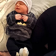 James is registered to the contest to win money with this photo: baby, sleeping, hat, sweater, batman_logo, socks, bed, blanket, person, infant, cozy, cute, resting, soft_fabric, hand, leg, indoor, child, newborn, clothing
