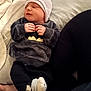 baby, sleeping, hat, sweater, batman_logo, socks, bed, blanket, person, infant, cozy, cute, resting, soft_fabric, hand, leg, indoor, child, newborn, clothing