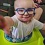 baby, child, glasses, walker, smile, indoor, couch, toy, person, blue_shirt, living_room, furniture, hand, curious, young_child, playful, infant, seat, face, happy