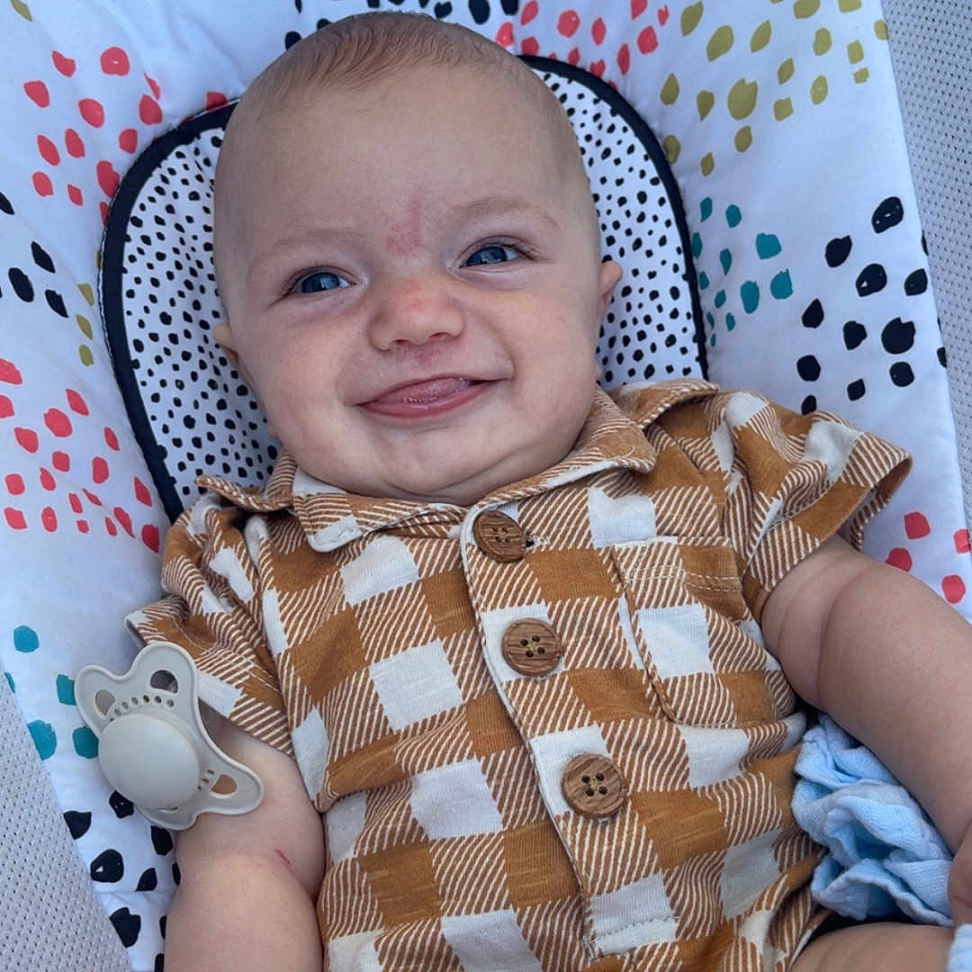 Wilbur joined the competition — help win amazing prizes! baby, blue_eyes, checkered_clothing, child, closeup, cushion, cute, happy, indoors, infant, pacifier, patterned_fabric, plush, portrait, relaxed, short_hair, sitting, smile, soft_toys, tongue