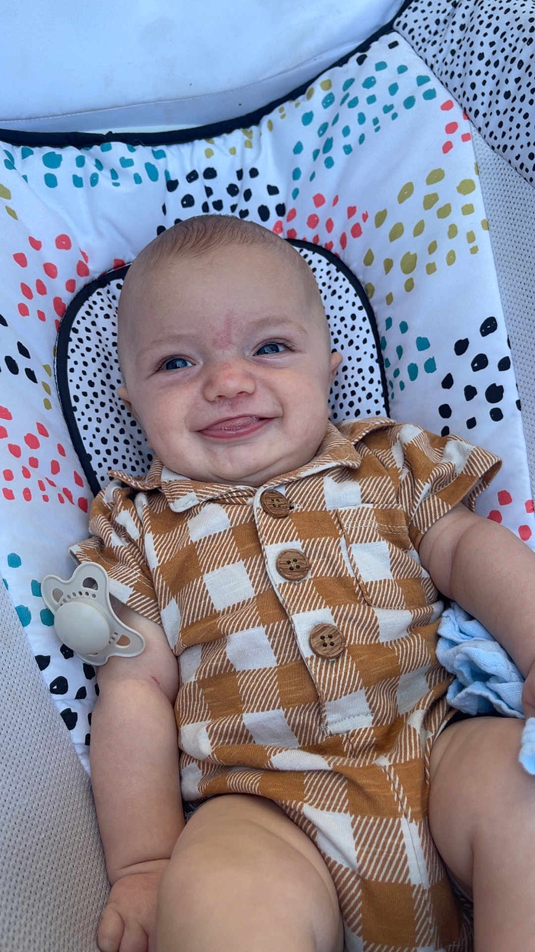 Wilbur joined the competition — help win amazing prizes! baby, infant, smile, tongue, checkered_clothing, pacifier, cushion, patterned_fabric, blue_eyes, short_hair, sitting, cute, happy, indoors, child, plush, soft_toys, relaxed, closeup, portrait