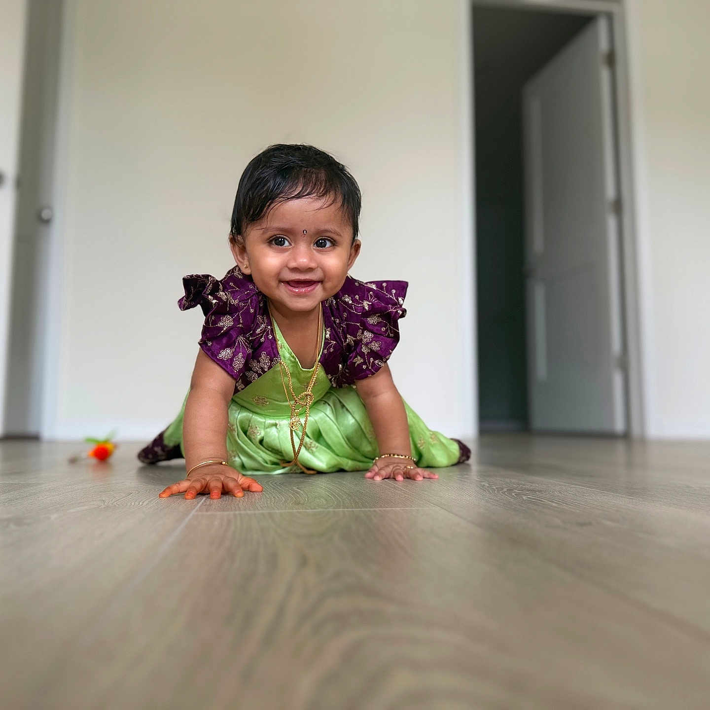 Vaibhavi joined the competition — help win amazing prizes! baby, child, crawling, cute, door, floor, flooring, gold_jewelry, green, happy, home, indoor, person, portrait, purple, smiling, toddler, traditional_clothing, wooden_floor, young