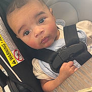 Tommy James is registered to the contest to win money with this photo: baby, child, car_seat, seatbelt, key, wooden_table, indoor, curious, infant, safety, light_glare, face, person, young_child, clothing, hand, closeup, seat, warning_label, expression