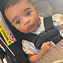 baby, child, car_seat, seatbelt, key, wooden_table, indoor, curious, infant, safety, light_glare, face, person, young_child, clothing, hand, closeup, seat, warning_label, expression