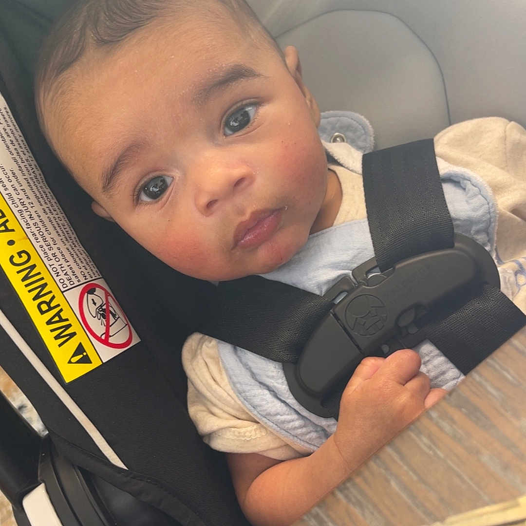 Tommy James is registered to the contest to win money with this photo: baby, car_seat, child, closeup, clothing, curious, expression, face, hand, indoor, infant, key, light_glare, person, safety, seat, seatbelt, warning_label, wooden_table, young_child