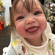 Penelope joined the competition — help win amazing prizes! baby, toddler, smile, tongue_out, bib, highchair, closeup, face, eyes, bangs, hair, rosy_cheeks, indoor, christmas_tree, holiday_decor, chair, expression, cute, portrait, playful