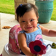 Amari is registered to the contest to win money with this photo: baby, blue_dress, brick_pillar, child, cute, flower_toy, greenery, hair_clip, happy, outdoor, person, pink_cushion, planter, playtime, porch, smile, sunlight, toddler, toy, walker
