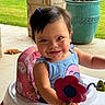 baby, blue_dress, brick_pillar, child, cute, flower_toy, greenery, hair_clip, happy, outdoor, person, pink_cushion, planter, playtime, porch, smile, sunlight, toddler, toy, walker