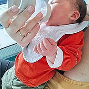 Augustin a rejoint le concours — aidez-le/la à gagner de superbes lots ! baby, feeding, bottle, bib, orange_sweater, green_pants, adult_hand, indoor, window, radiator, closeup, infant, person, clothing, holding, feeding_time, peaceful, cute, newborn, parent