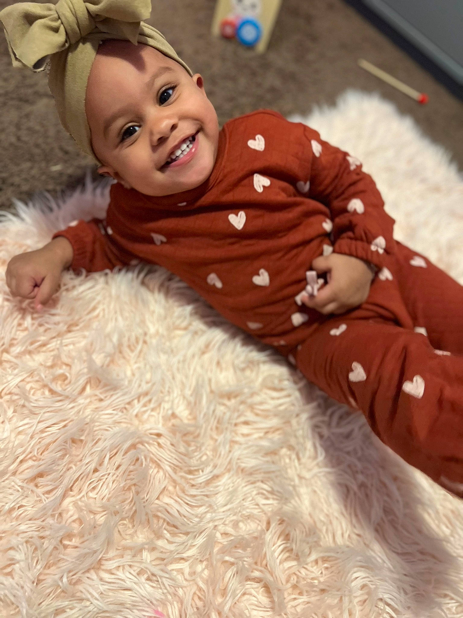 Sunni is registered to the contest to win money with this photo: baby, baby_toddler_clothing, cheek, child, face, flooring, fun, fur, fur_clothing, happy, headgear, headwear, joy, pattern, peach, person, sitting, sleeve, smile, toddler
