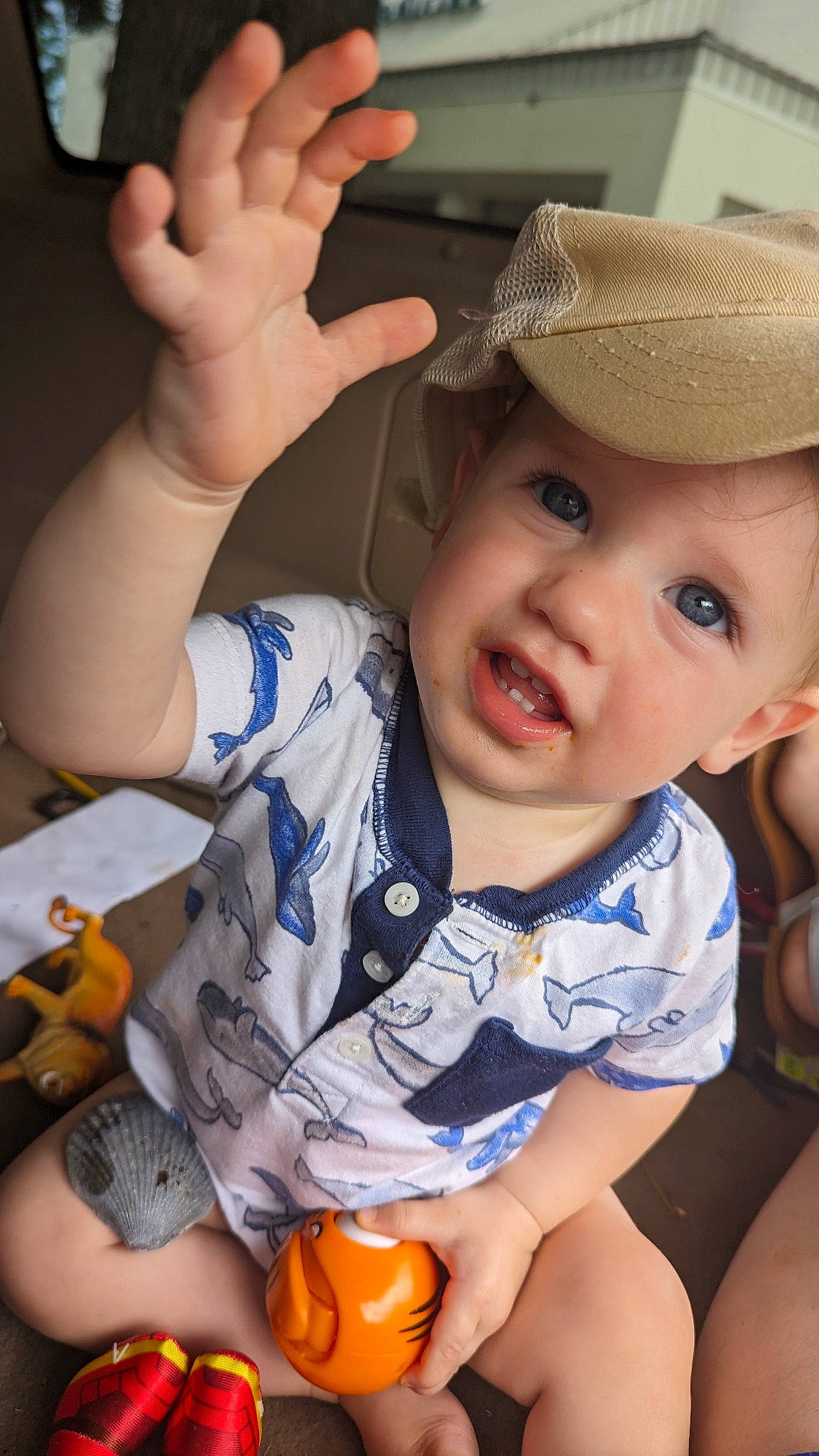 Killian is registered to the contest to win money with this photo: arm, baby, baby_toddler_clothing, cap, facial_expression, finger, gesture, hairstyle, hand, happy, headwear, iris, lip, mouth, nose, orange, organ, person, photograph, skin