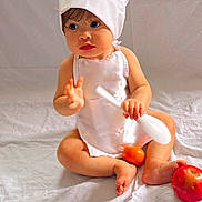 Hellena is registered to the contest to win money with this photo: baby, child, chef_hat, white_apron, sitting, spoon, orange_fruit, apple, barefoot, curious, indoor, white_background, cute, portrait, infant, soft_lighting, food, playful, young_child, closeup