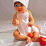 baby, child, chef_hat, white_apron, sitting, spoon, orange_fruit, apple, barefoot, curious, indoor, white_background, cute, portrait, infant, soft_lighting, food, playful, young_child, closeup