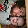 baby, man, beard, face, smile, close_up, indoor, person, child, casual_clothing, graphic_tee, polka_dot, bow_tie, hand, affection, selfie, lying_down, skin, blue_eyes, tender_moment