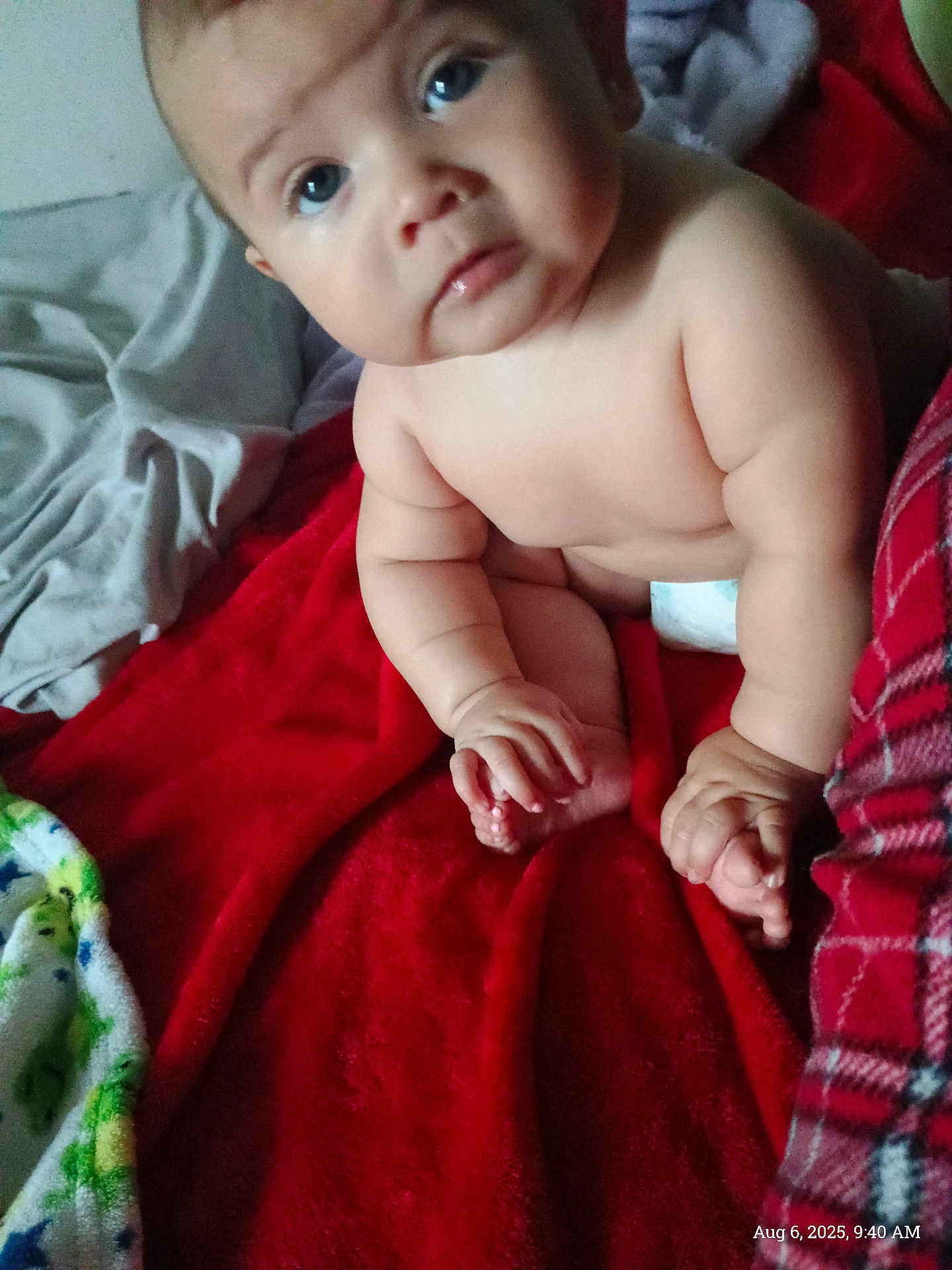 Bella is registered to the contest to win money with this photo: baby, child, infant, blanket, red_blanket, diaper, skin, hand, foot, face, eyes, indoors, soft_texture, plush, cute, chubby, sitting, curious, person, home