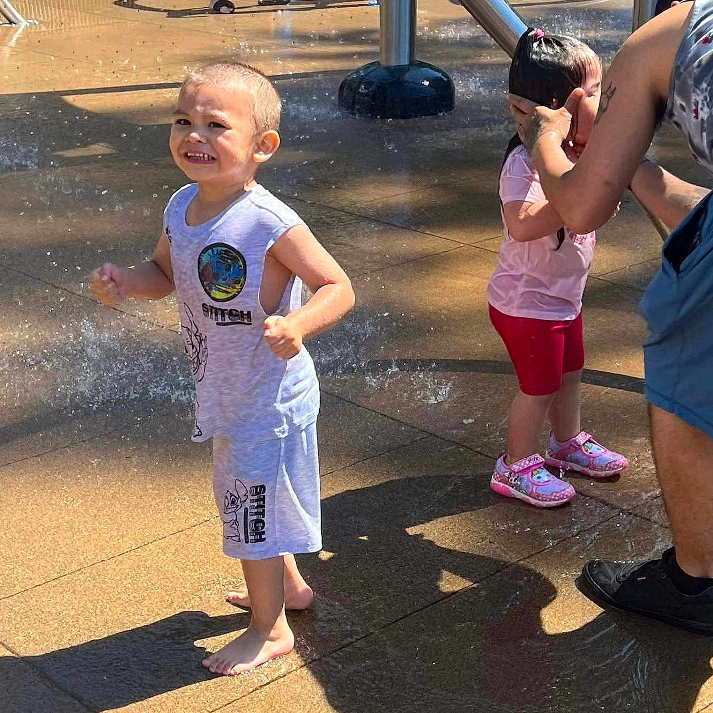 Nathaniel Truncer is registered to the contest to win money with this photo: adult, barefoot, boy, child, clothing, concrete, family, fun, girl, happy, outdoor, playground, shadow, shoes, splash_pad, summer, sunlight, tattoo, water, water_spray