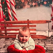 Gabriel a rejoint le concours — aidez-le/la à gagner de superbes lots ! baby, child, infant, smile, red_cushion, candy_cane, wooden_bench, sleigh, bokeh, snow, cobblestone_floor, striped_shirt, portrait, holiday, christmas, cute, props, indoors, festive, background