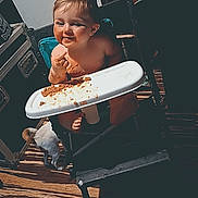 Dustin is registered to the contest to win money with this photo: baby, child, clothing, cute, face, food, furniture, happy, high_chair, indoor, meal, mess, messy, person, seat, smile, toddler, tray, wooden_floor, young_child