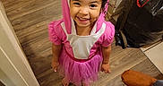 Jowhara is registered to the contest to win money with this photo: barefoot, child, corner, costume, curly_hair, cute, flooring, happy, home, indoor, person, pink, playful, shark_hood, smiling, trash_bag, tutu, wall, wooden_floor, young_child