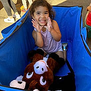 Jowhara joined the competition — help win amazing prizes! child, smiling, curly_hair, blue_wagon, stuffed_animal, outdoor, sunlight, people, legs, casual_clothing, happy, playful, toy, fabric, sneakers, concrete, daylight, person, cute, kid