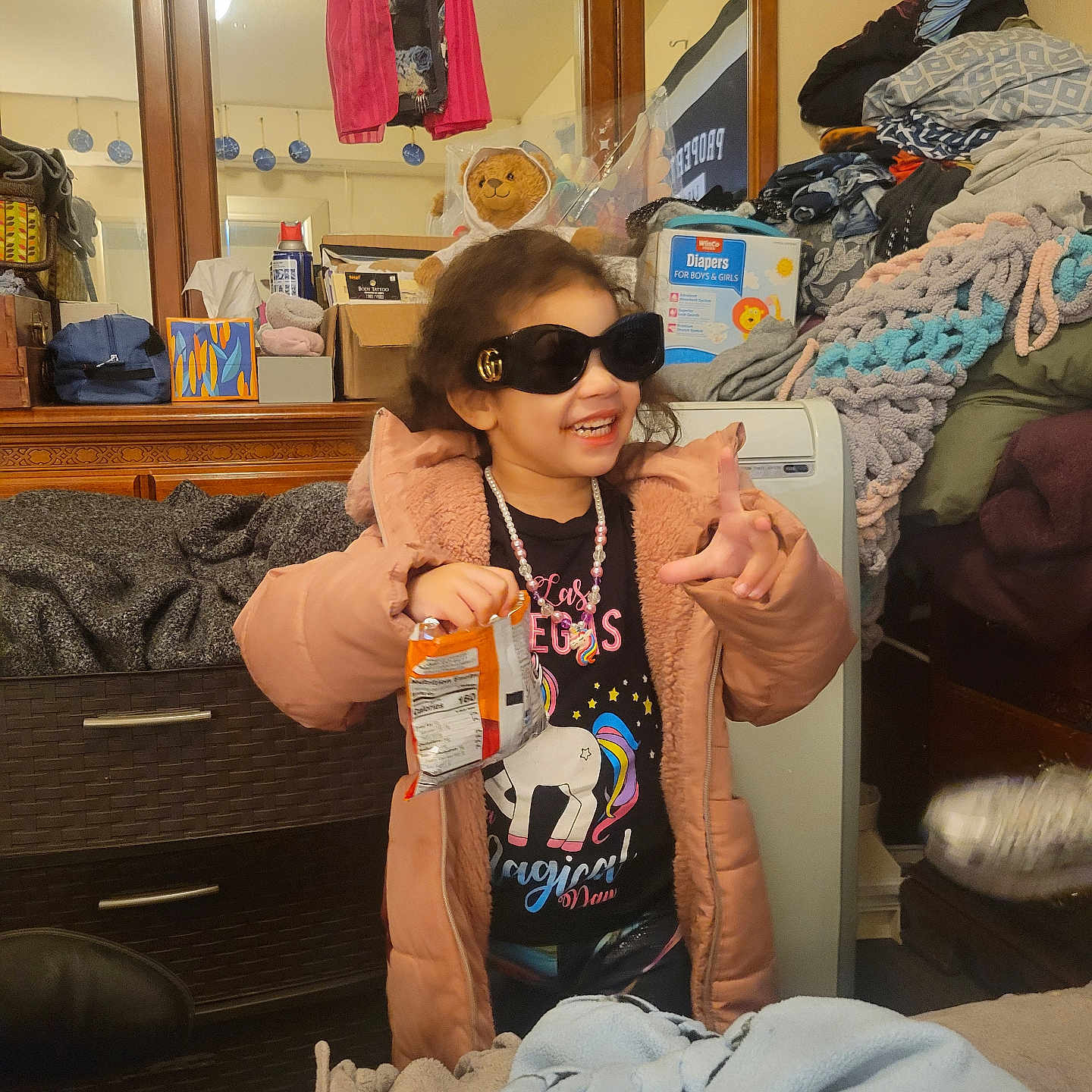 Jowhara is registered to the contest to win money with this photo: child, girl, sunglasses, jacket, snack, smile, indoor, clothing, teddy_bear, mirror, furniture, blanket, drawer, room, cozy, happy, person, casual, playful, accessory