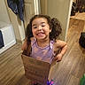 Jowhara joined the competition — help win amazing prizes! child, girl, smiling, cardboard_box, curly_hair, purple_dress, sneakers, light_up_shoes, indoor, wooden_floor, door, toddler, happy, playful, flooring, household, home, person, cute, fun
